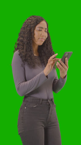 Vertical-Video-Three-Quarter-Length-Shot-Of-Vertical-Video-Woman-Waiting-Looking-At-Mobile-Phone-Against-Green-Screen